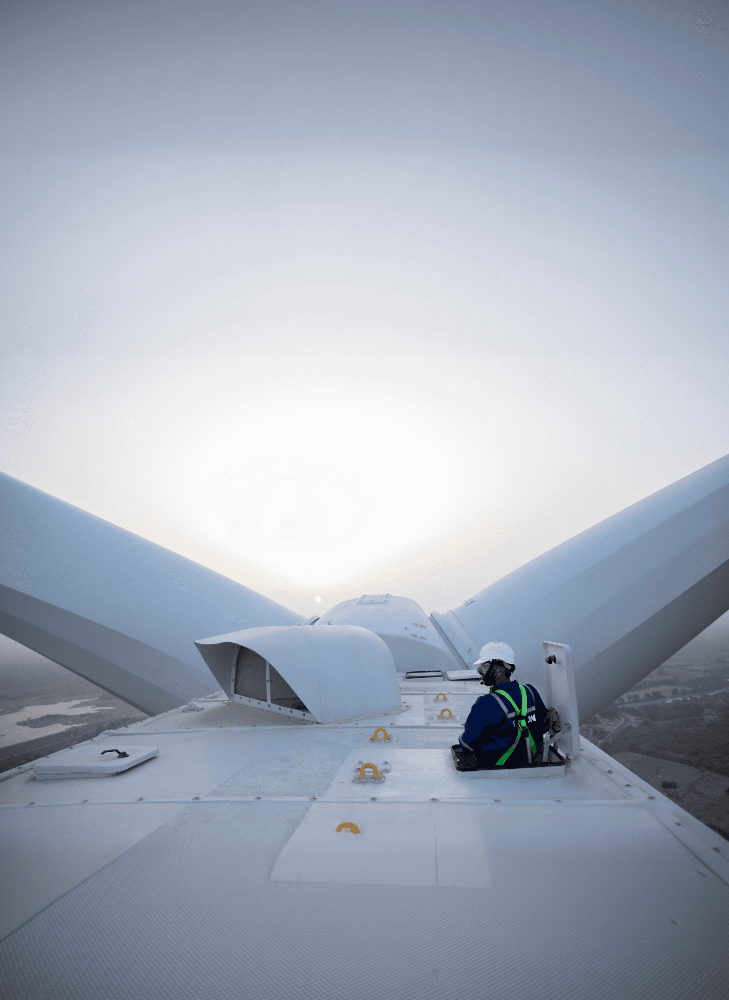 Wind turbine technician on the nacelle with blades framing the horizon at sunrise