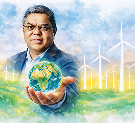 Tulsi Tanti holding a globe before a field of turbines